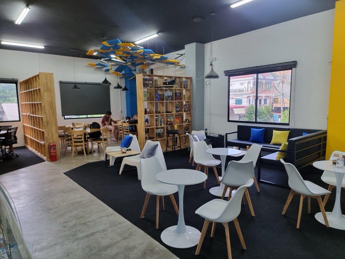 Inside Level Up — board-game shelves, coworking screen and lounge seating under the hexagon light rig