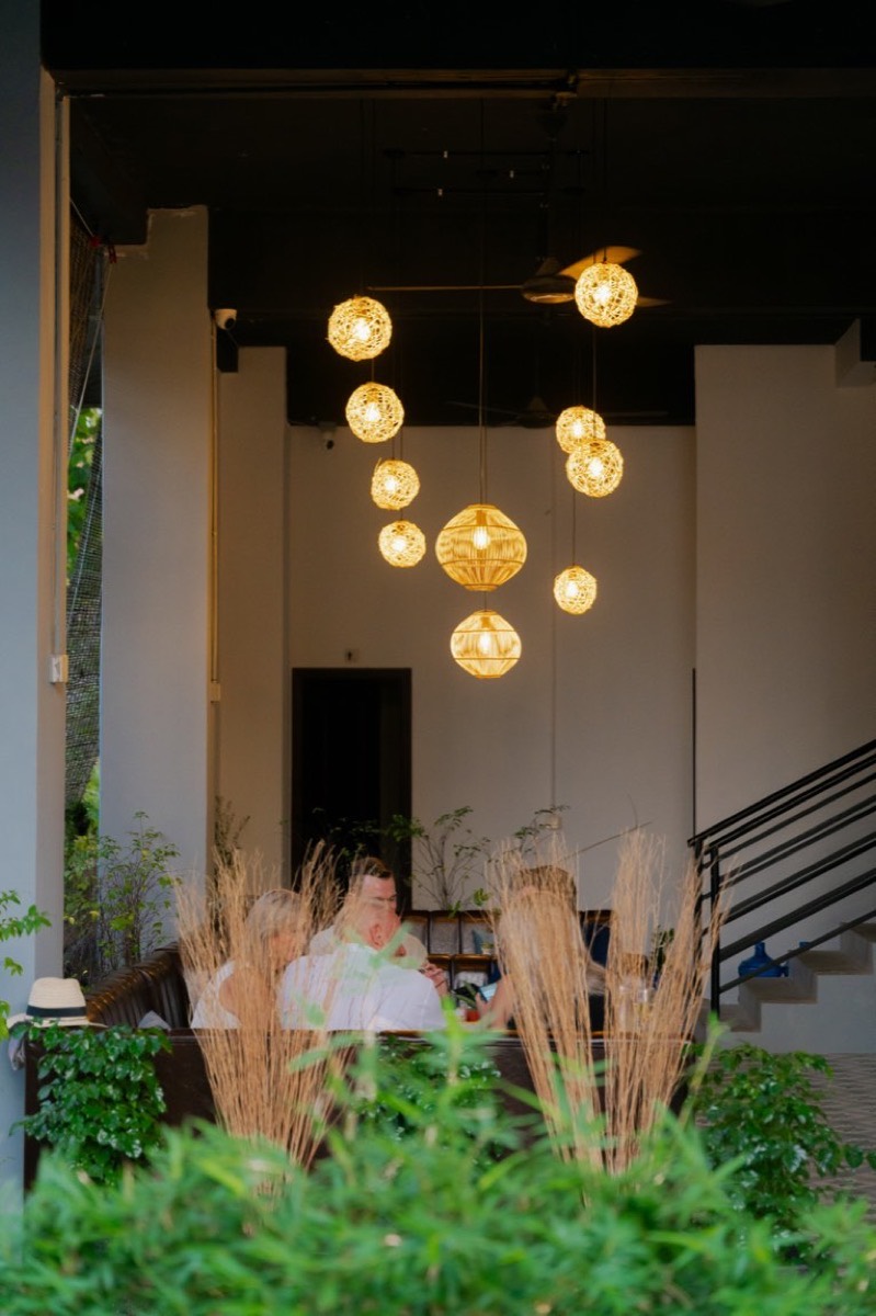 Nomad at dusk — clustered rattan lanterns over booth seating framed by plants